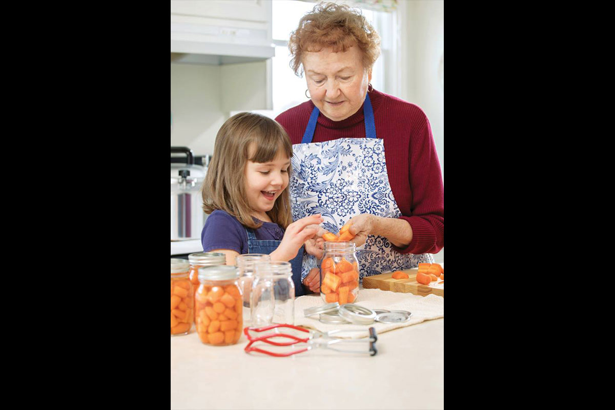 young girl helping her grandmother can food