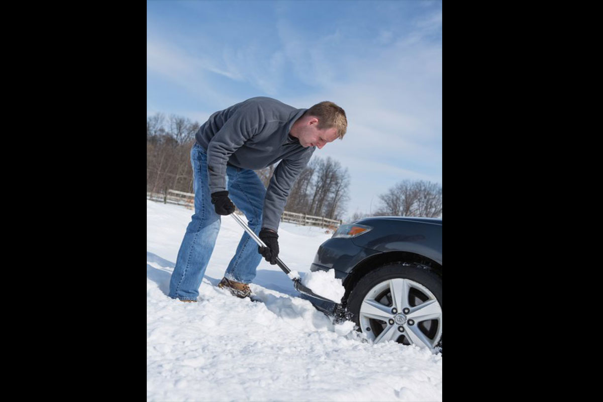 man shoveling snow in front of his car