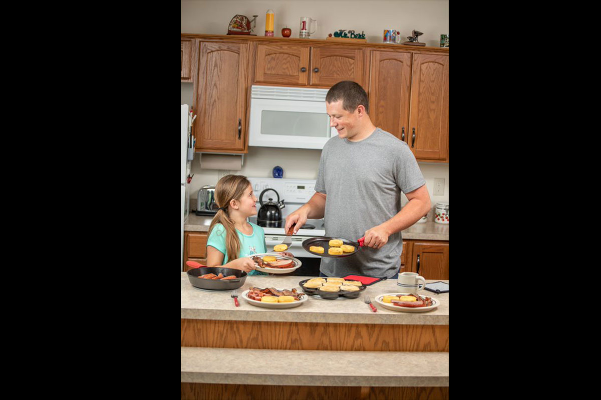 Man preparing traditional breakfast with his daughter on cast iron cookware.