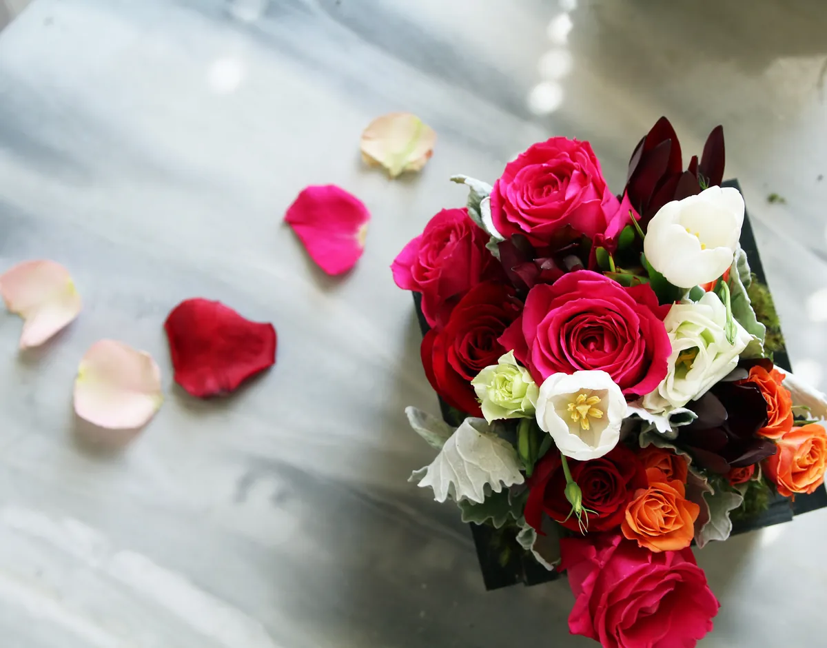A floral arrangement of roses and white tulips in a wood box, with scattered petals